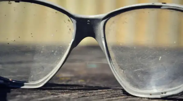 Brudne okulary ochronne leżą na drewnianej powierzchni. Czas na polerowanie okularów, by znów były przejrzyste.