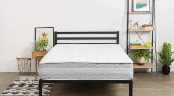 A white and gray mattress on a black metal bed frame. This is one of the mattresses to avoid if you want a good night's sleep.