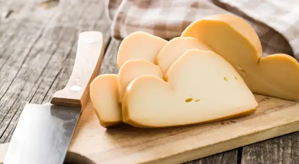Tagli di **la provola** affumicata su un tagliere di legno, accanto a un coltello.