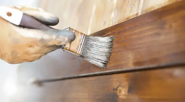 Main gauche gantée appliquant du vernis sur des lattes de bois brun pour vernir un meuble.