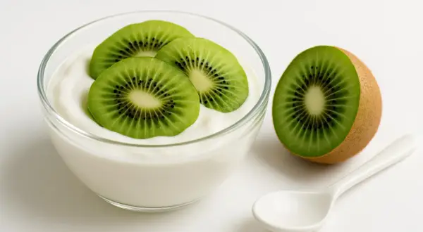 Yogurt con kiwi, un'ottima scelta tra gli alimenti che assorbono i gas intestinali. Una fetta di kiwi accanto a una ciotola di yogurt bianco con tre fette di kiwi sopra.