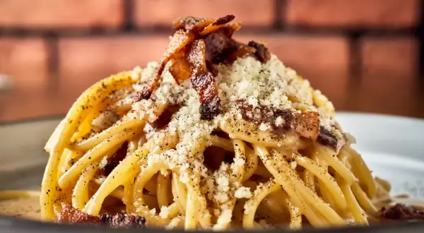 Pyszne spaghetti carbonara, klasyka włoskich przepisów na makaron, posypane parmezanem i chrupiącym boczkiem.