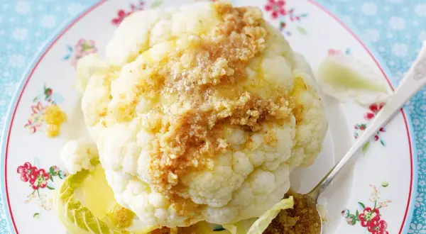 Ganzes Blumenkohlröschen mit Butter und Bröseln beträufelt, serviert auf einem Teller mit Blumenmuster. Tolle Idee für Blumenkohl Rezepte!