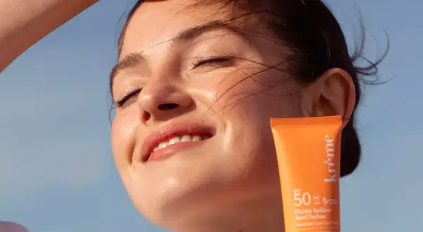 Une jeune femme rayonne sous le soleil, protégeant sa peau avec un fluide solaire. Un rappel : mettre de la crème solaire tous les jours pour une peau éclatante.