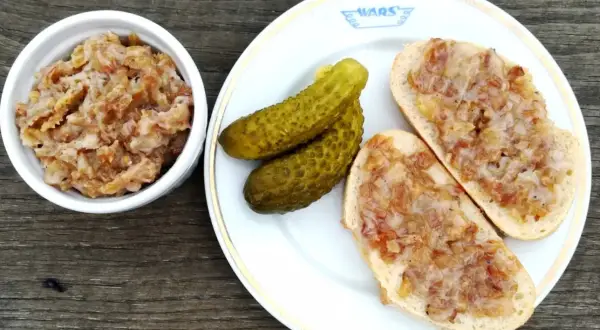 Smalec z cebulą i jabłkiem w miseczce, na talerzu kromki chleba ze smalcem i ogórki kiszone.