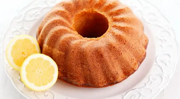 Puszysta babka cytrynowa siostry Anastazji, lekko zarumieniona, z dwoma plasterkami cytryny na ozdobnym talerzu.