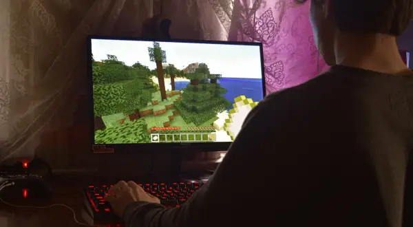 Gracz wciela się w postać w grze Minecraft, eksplorując zielony świat. W tle widać zasłony.