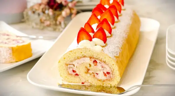 Eine köstliche Biskuitrolle mit Erdbeerfüllung, verziert mit frischen Erdbeeren und Sahnetupfern. Ein Klassiker, der an Omas Biskuitrolle Landfrauen erinnert.