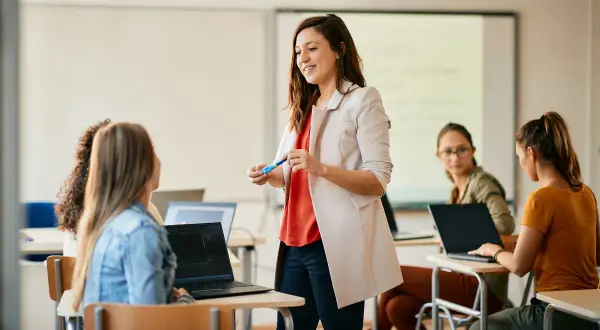 Nauczycielka wita studentów, omawiając jak zostać nauczycielem. W sali lekcyjnej panuje atmosfera nauki i zaangażowania.