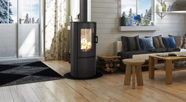 Gemütliches Wohnzimmer mit brennendem Kaminofen (BimschV Stufe 2 Liste), Holzstapel, Sofa mit Kissen und Holztisch.