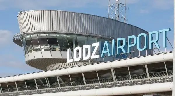 Budynek lotniska w Łodzi z napisem "ŁÓDŹ AIRPORT" na niebieskim niebie.