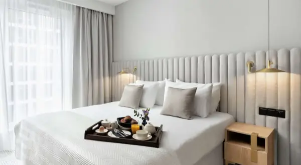 Eleganckie łóżko w pokoju hotelowym, śniadanie na tacy, jak w Royal Tulip Warszawa.