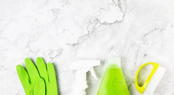 Guanti verdi, spray bianco, flacone di liquido verde e spazzola gialla pronti per scoprire come pulire pietra.