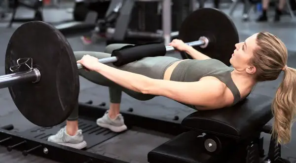Kobieta wykonuje hip thrust z obciążeniem na ławce. Ćwiczenie to świetnie wzmacnia pośladki i jest możliwe do wykonania nawet w domu.