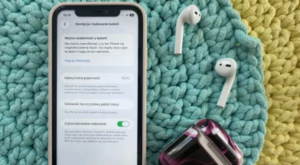 Jak sprawdzić pojemność baterii iPhone'a? Na ekranie widać 100% maksymalnej pojemności baterii, obok słuchawek AirPods.