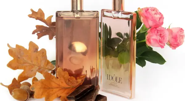 Dwa flakony Lancôme Idôle, jeden z jesiennymi liśćmi i żołędziami, drugi z różowymi różami.