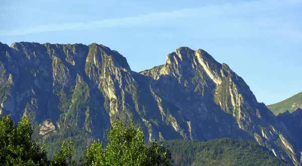 Majestatyczny Giewont, niczym śpiący rycerz, wznosi się na tle błękitnego nieba. Jego skaliste zbocza porośnięte zielenią tworzą imponujący krajobraz.