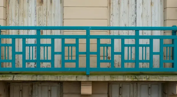Turkusowe, geometryczne mocowanie balustrady od czoła, z widocznymi odrapanymi drzwiami poniżej.