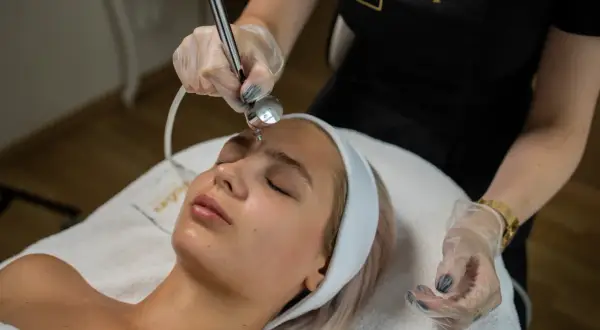 Zabieg dermaoxy na twarz młodej kobiety. Kosmetolog wykonuje zabieg urządzeniem, które rozpyla strumień tlenu i substancji aktywnych.
