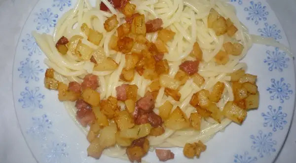 Makaron z ziemniakami i skwarkami na talerzu z niebieskim wzorem.