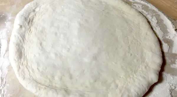 Pâte à pizza étalée sur une surface farinée, prête pour une recette pâte à pizza rapide.
