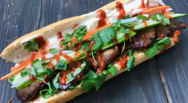 En saftig banh mi med tofu, färska grönsaker och en härlig sås på en träbakgrund.