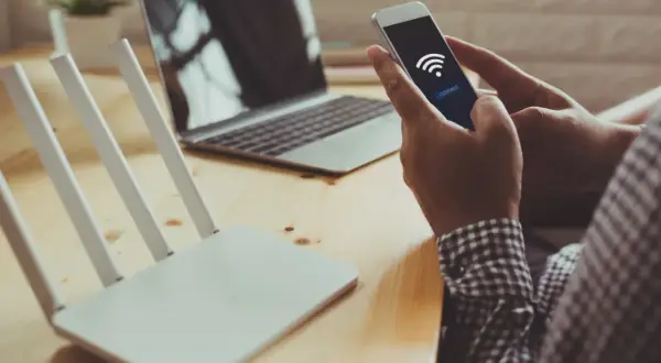 Dłoń trzyma smartfon z ikoną Wi-Fi i przyciskiem "connect", obok router i laptop. Szybkie połączenie dzięki wifi direct.