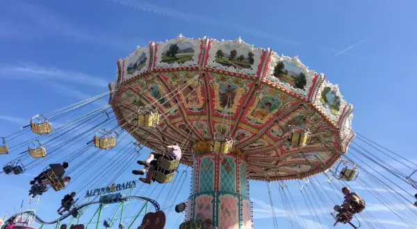 Carrusel giratorio en un oktoberfest parque de atracciones, con gente disfrutando del paseo bajo un cielo azul.