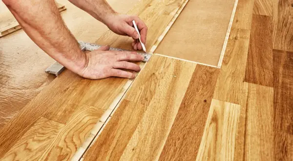 Un bricoleur utilise une règle et un crayon pour marquer une ligne de coupe sur du parquet flottant, étape essentielle pour savoir comment couper du parquet flottant.