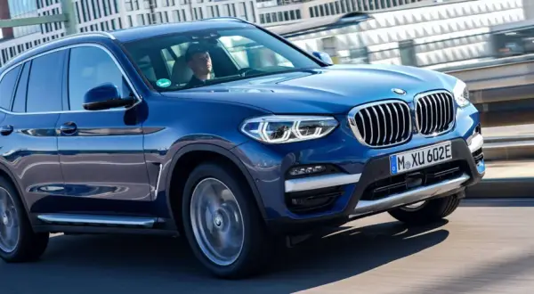 Niebieskie BMW X3 w ruchu miejskim. Zastanawiasz się, ile kosztuje BMW X3? Ten model wygląda na nowy i luksusowy.