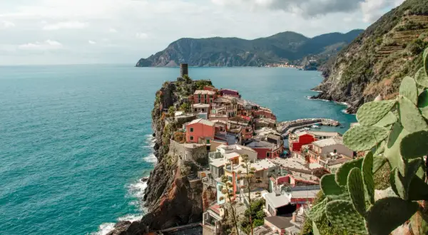 Pueblo costero de casas coloridas en un acantilado, con el mar azul y montañas al fondo. Un lugar que evoca la esencia de la spezia el ejido.