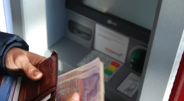 Ręce trzymają portfel i banknoty przy bankomacie. Czy rodzic może wypłacić pieniądze z konta dziecka?