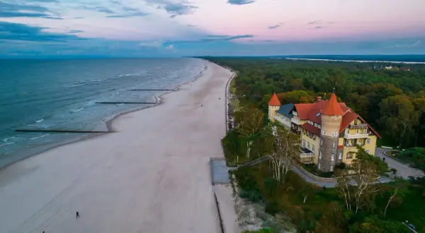 Zachód słońca nad morzem, piaszczysta plaża i zabytkowy budynek z wieżą w Łebie.