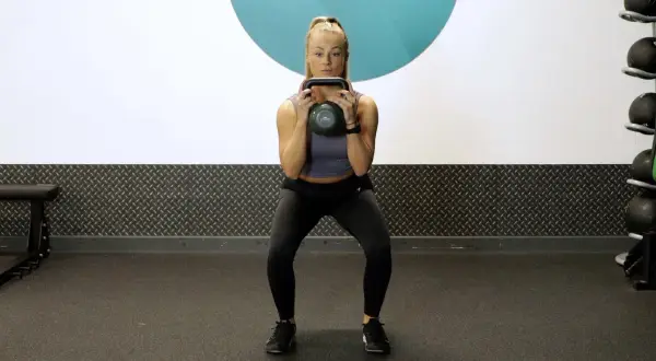 Woman performing kettlebell squat pulses in a gym.