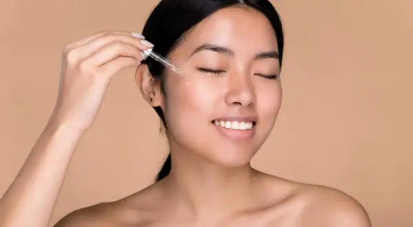 Donna applica acido ialuronico sul viso con un contagocce per una pelle idratata e luminosa.