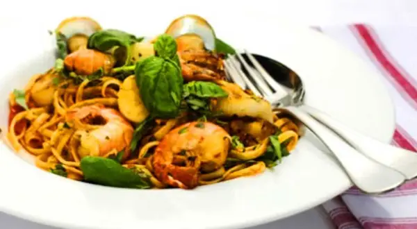 En tallrik med linguine frutti di mare, toppad med färska örter och serverad med bestick.