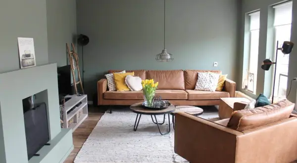Gemütliches Wohnzimmer mit braunen Ledermöbeln und einer besonderen Wandgestaltung in Salbeigrün. Gelbe Tulpen auf dem Couchtisch.