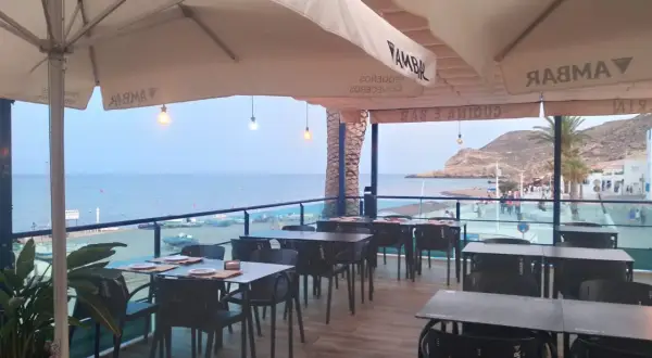 Terraza de restaurante con mesas y sillas, vistas al mar y a la playa. Un lugar ideal para disfrutar de un socorrito las negras al atardecer.
