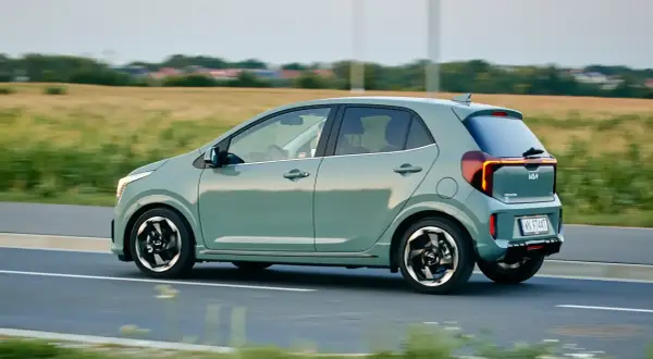 Zielony Kia Picanto w ruchu drogowym, widok z boku, z polem w tle.