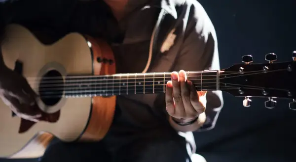 Person übt das Spielen einer akustik gitarre. Hände formen Akkorde auf dem Griffbrett, während die andere Hand die Saiten anschlägt.