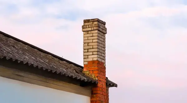 Mokry komin na strychu, z cegły, częściowo zniszczony, na tle nieba.