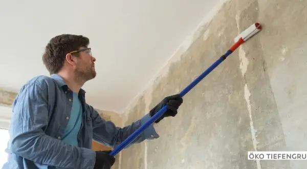 Mann mit Schutzbrille trägt eine Grundierung auf eine rohe Wand auf, um sie für die weitere Bearbeitung vorzubereiten.