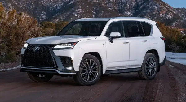 Biały Lexus LX 600 na drodze gruntowej, z ośnieżonymi górami w tle.