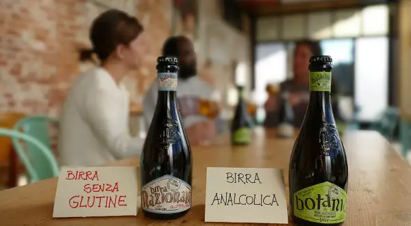 Bottiglie di birra sul tavolo. Una indica "Birra senza glutine", l'altra "Birra analcolica". Attenzione: la birra contiene lattosio.