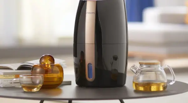 Elegancki nawilżacz ewaporacyjny Philips, obok szklanej filiżanki z herbatą i ozdobnej buteleczki. Czy do nawilżacza ewaporacyjnego można dodać olejek?