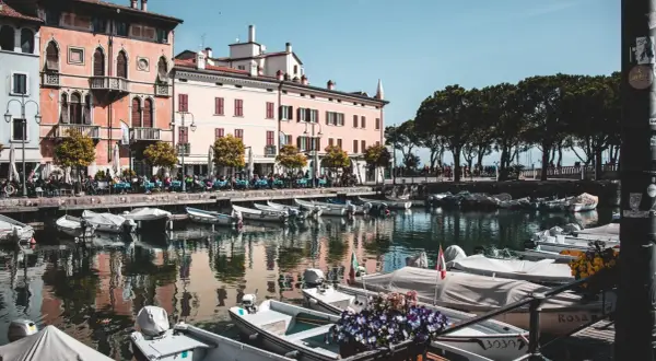 Barche ormeggiate nel porto di Desenzano del Garda, con edifici colorati e alberi sullo sfondo.