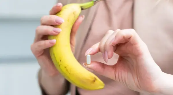 Dłoń trzymająca banana i kapsułkę, sugerującą potas najlepiej przyswajalny z natury i suplementów.