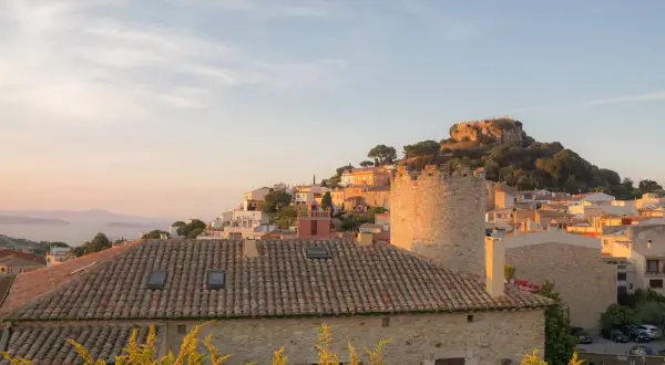 Sonnenuntergang über einem Dorf an der Girona Costa Brava. Ein alter Turm und ein Schloss auf einem Hügel über weiß getünchten Häusern.