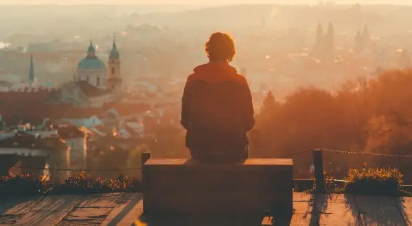 Osoba siedzi na ławce, patrząc na miasto w zachodzącym słońcu. Może to być moment refleksji nad zespołem pomijania stronnego.