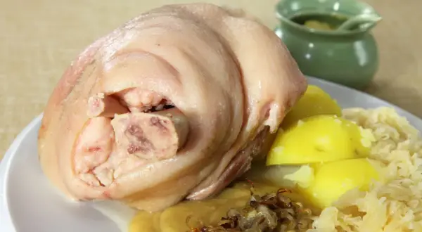 Ein deftiges, gekochtes Eisbein mit Salzkartoffeln, Sauerkraut und einer kleinen Schale mit Soße.